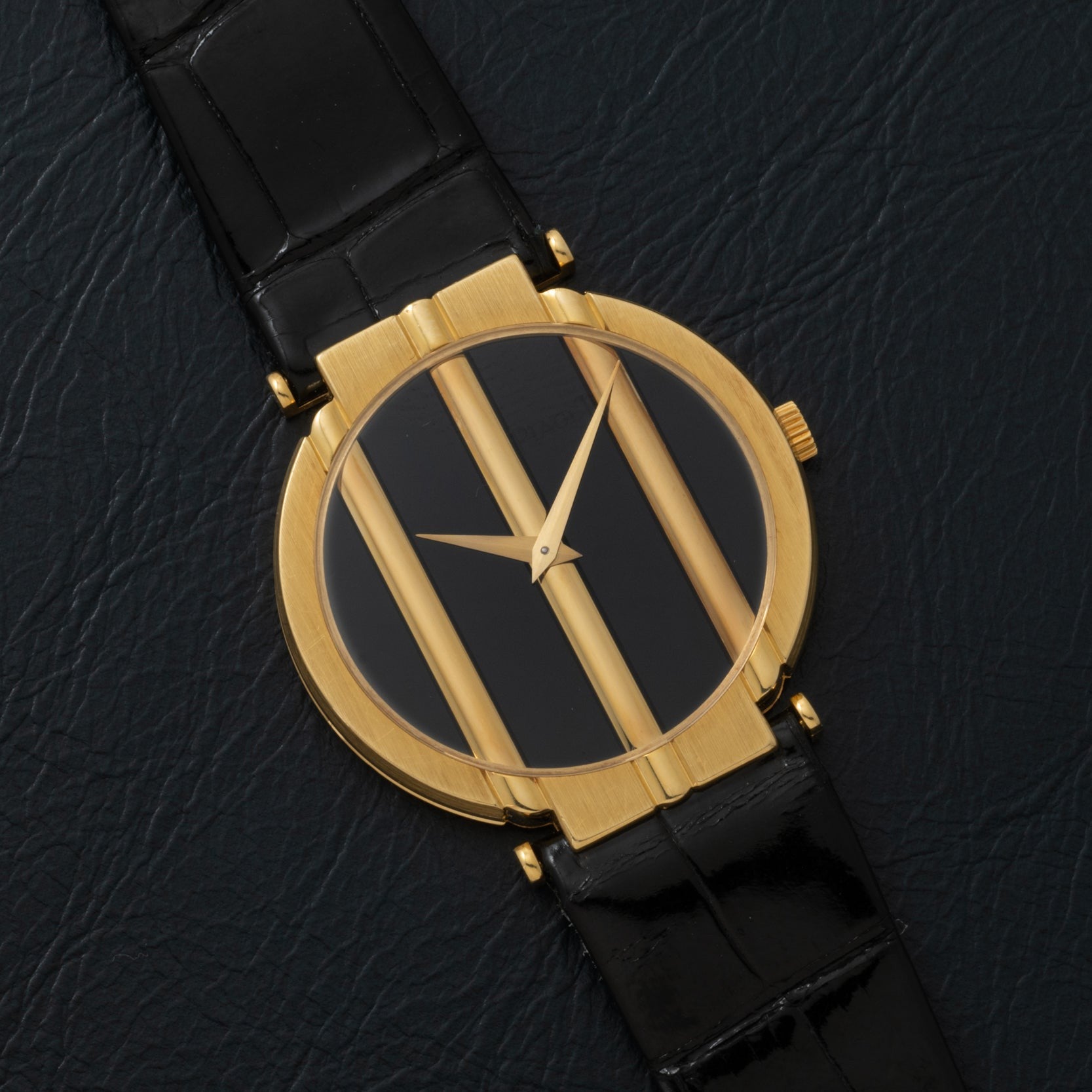 The Piaget Polo Onyx gold watch features a black face, three vertical gold bars, and a black leather strap, displayed on a textured black surface.