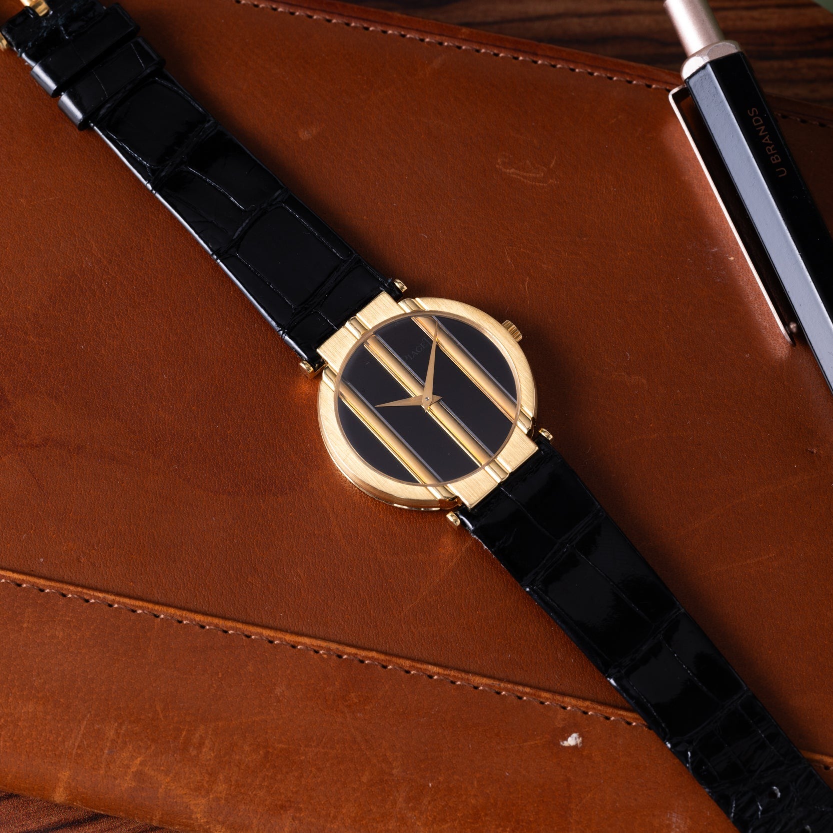 The Piaget Polo Onyx, a gold and black wristwatch with a geometric face, rests on a brown leather surface beside a pen.