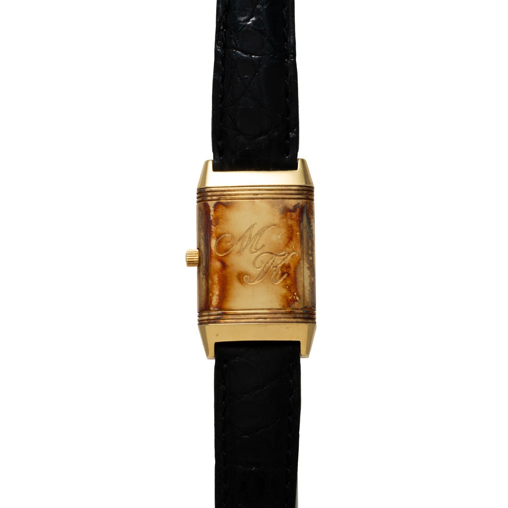 The Jaeger-LeCoultre Reverso Classique is a gold wristwatch featuring a brown-stained face, black leather strap, and engraved with the initials M K.