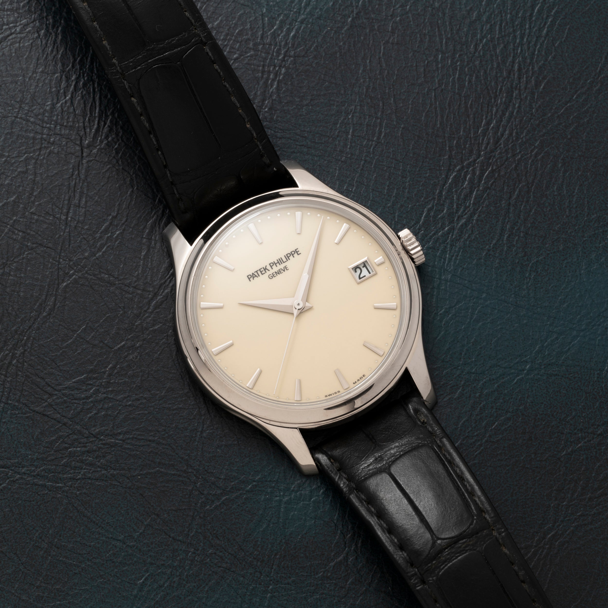 The Patek Philippe Calatrava, a silver wristwatch with a black leather band, rests on a dark textured surface.