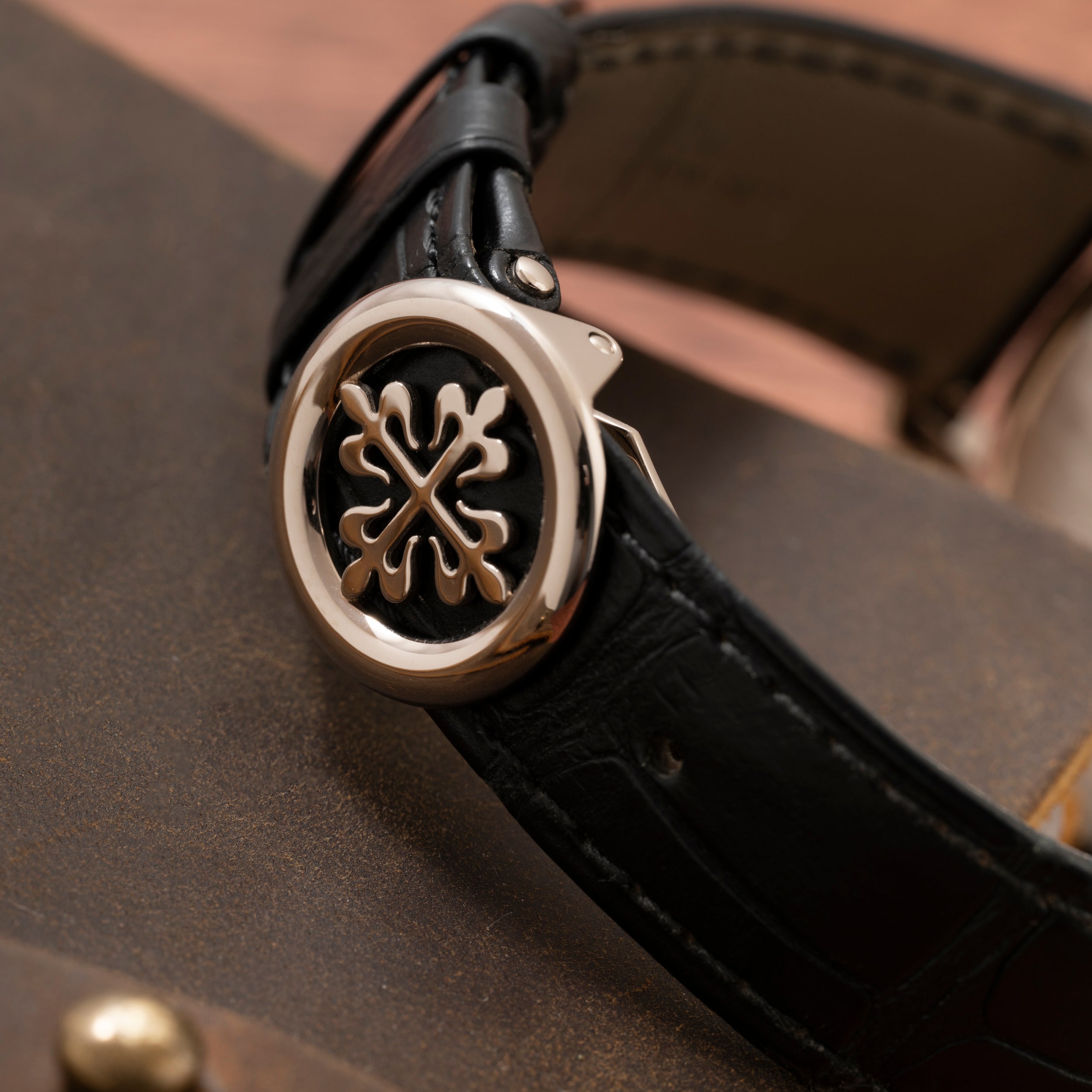 Close-up of a Patek Philippe Calatrava black leather watch strap with a round silver clasp featuring an ornate design.