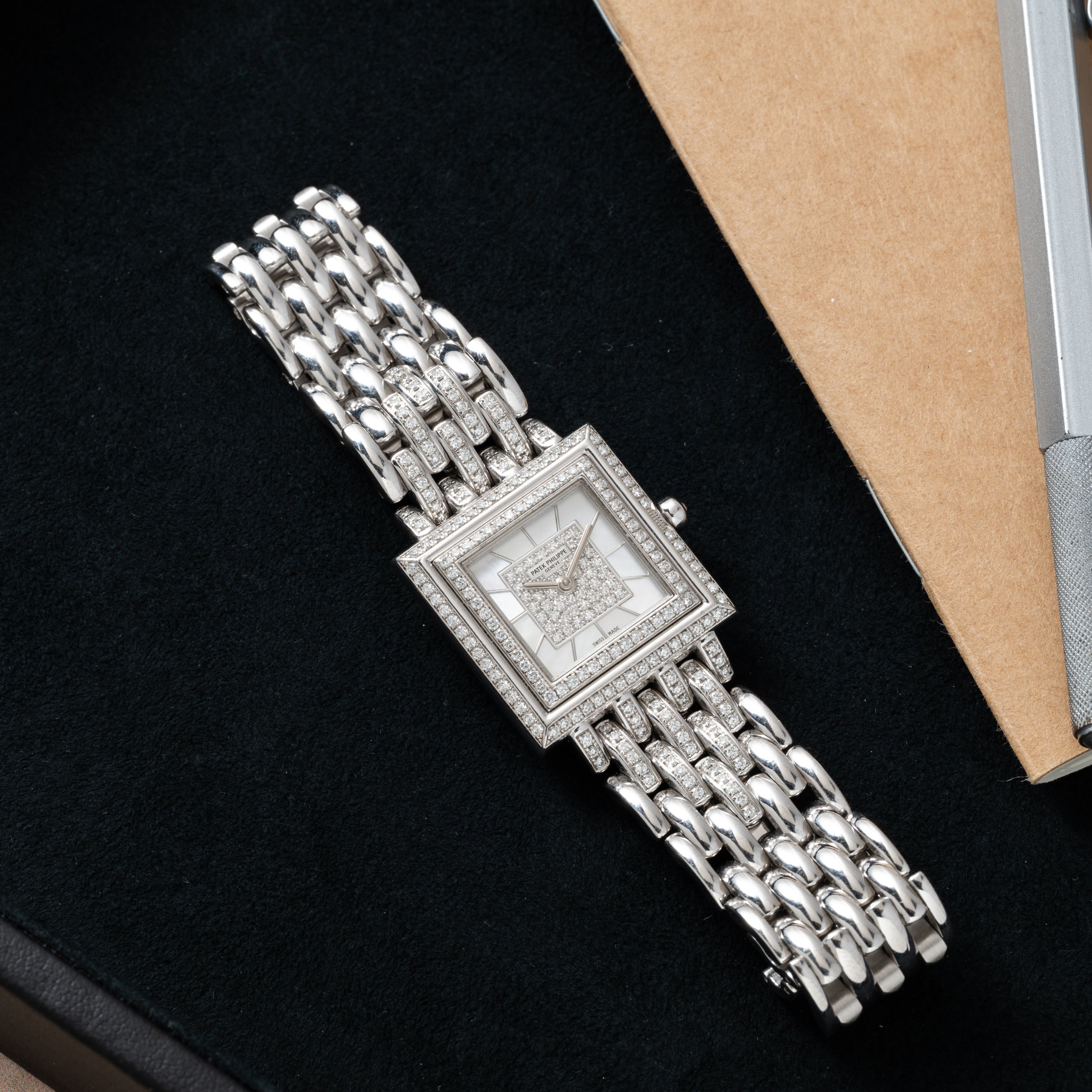 A Patek Philippe Gondolo silver wristwatch with diamond accents and a metal link band rests on a black surface.