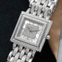 A square Patek Philippe Gondolo watch with diamond accents and a metal link band rests on a dark surface.