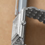 Close-up of the Patek Philippe Gondolo silver wristwatch with a metal band and diamond accents, displayed on a brown surface.
