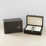 A Patek Philippe Aquanaut wristwatch rests in an open display box next to its sophisticated branded packaging.
