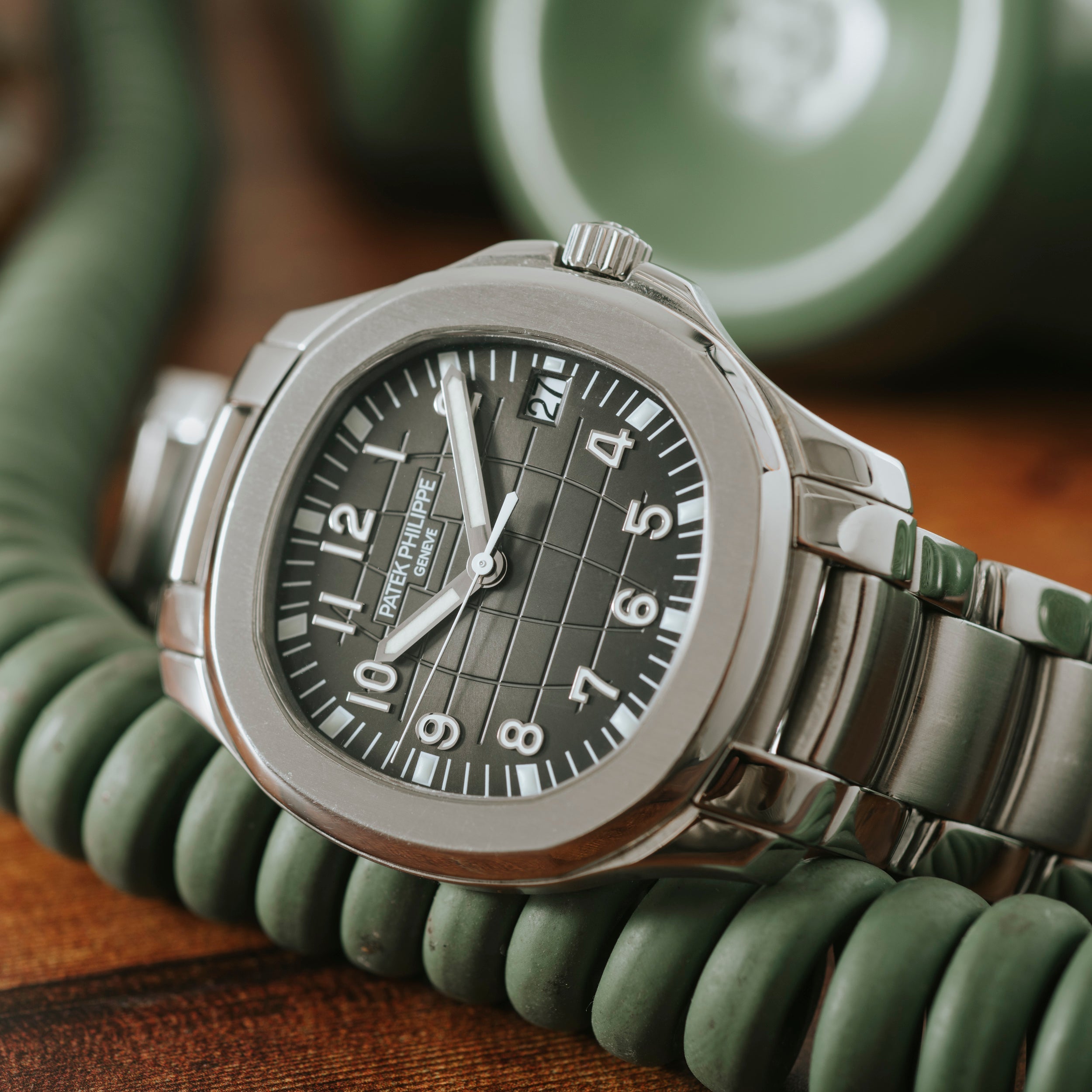 The Patek Philippe Aquanaut wristwatch with a dark green dial rests on a coiled green telephone cord.