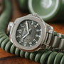 The Patek Philippe Aquanaut wristwatch with a dark green dial rests on a coiled green telephone cord.
