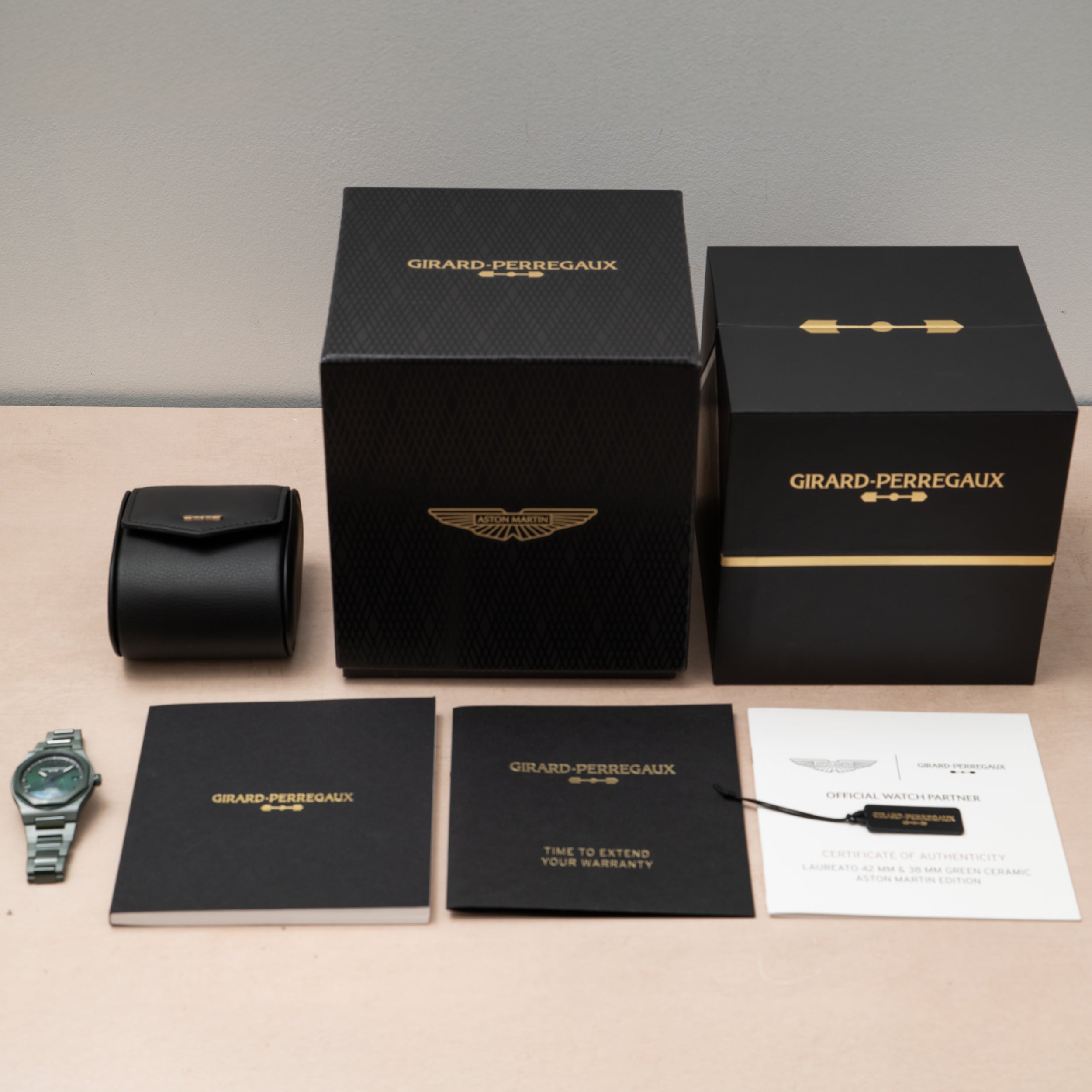 A Girard-Perregaux Laureato Green Ceramic Aston Martin Edition watch with its box, warranty card, booklet, and certificate on a table.
