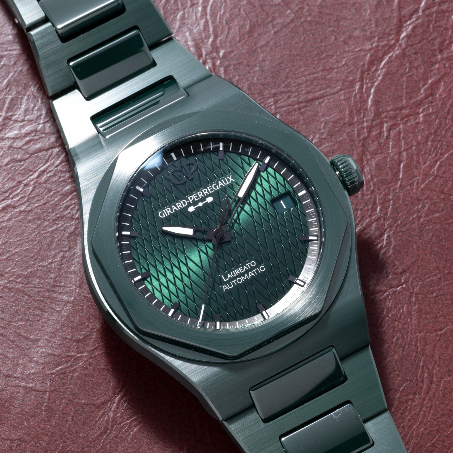 A Girard-Perregaux Laureato Green Ceramic Aston Martin Edition watch rests on a red leather surface.