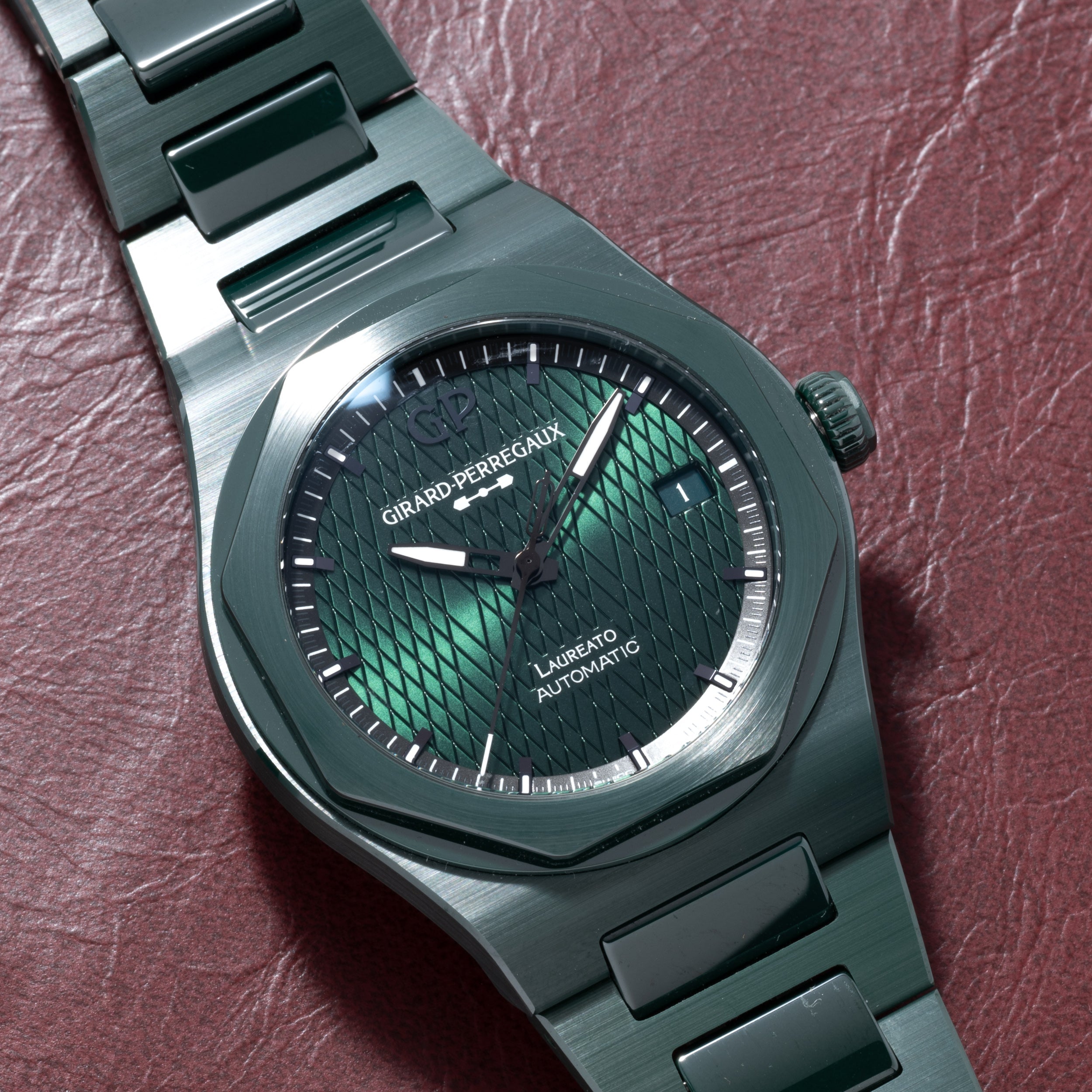 A Girard-Perregaux Laureato Green Ceramic Aston Martin Edition watch rests on a red leather surface.