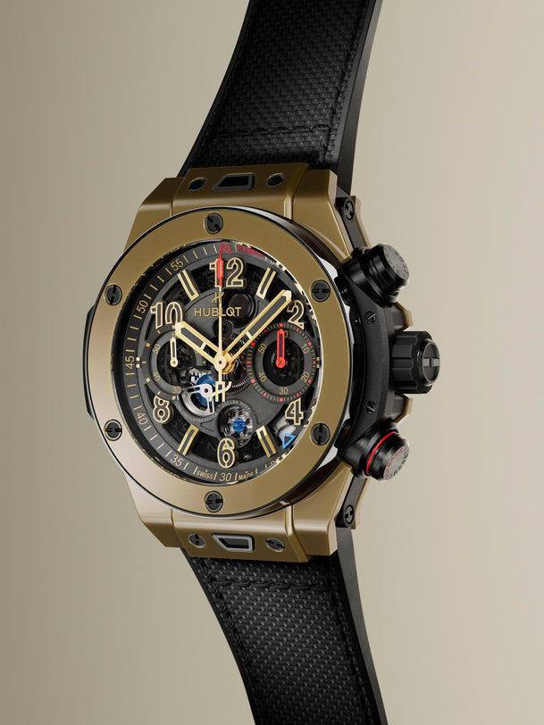 Gold-tone chronograph watch with black dial, gold hour markers, black rubber strap, and side pushers.