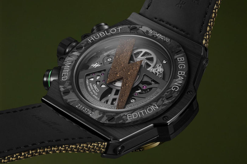 Black ceramic chronograph watch with exposed movement, brown dial detail, and black leather strap with gold stitching.