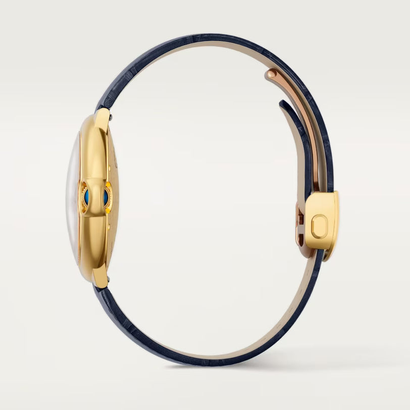 A side view of the slim Ballon Bleu De Cartier Watch by Cartier, featuring a gold case, dark blue leather strap, and a blue gemstone-accented crown, set against a plain light background.