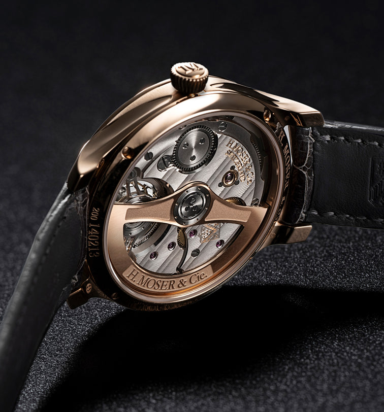 Rose gold tourbillon watch with open caseback, visible mechanical movement, black leather strap, and diamond-set bezel on dar