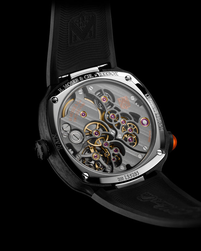 Luxury watch with visible mechanical movement, gold and silver gears, red crown, black rubber strap, and stainless steel case