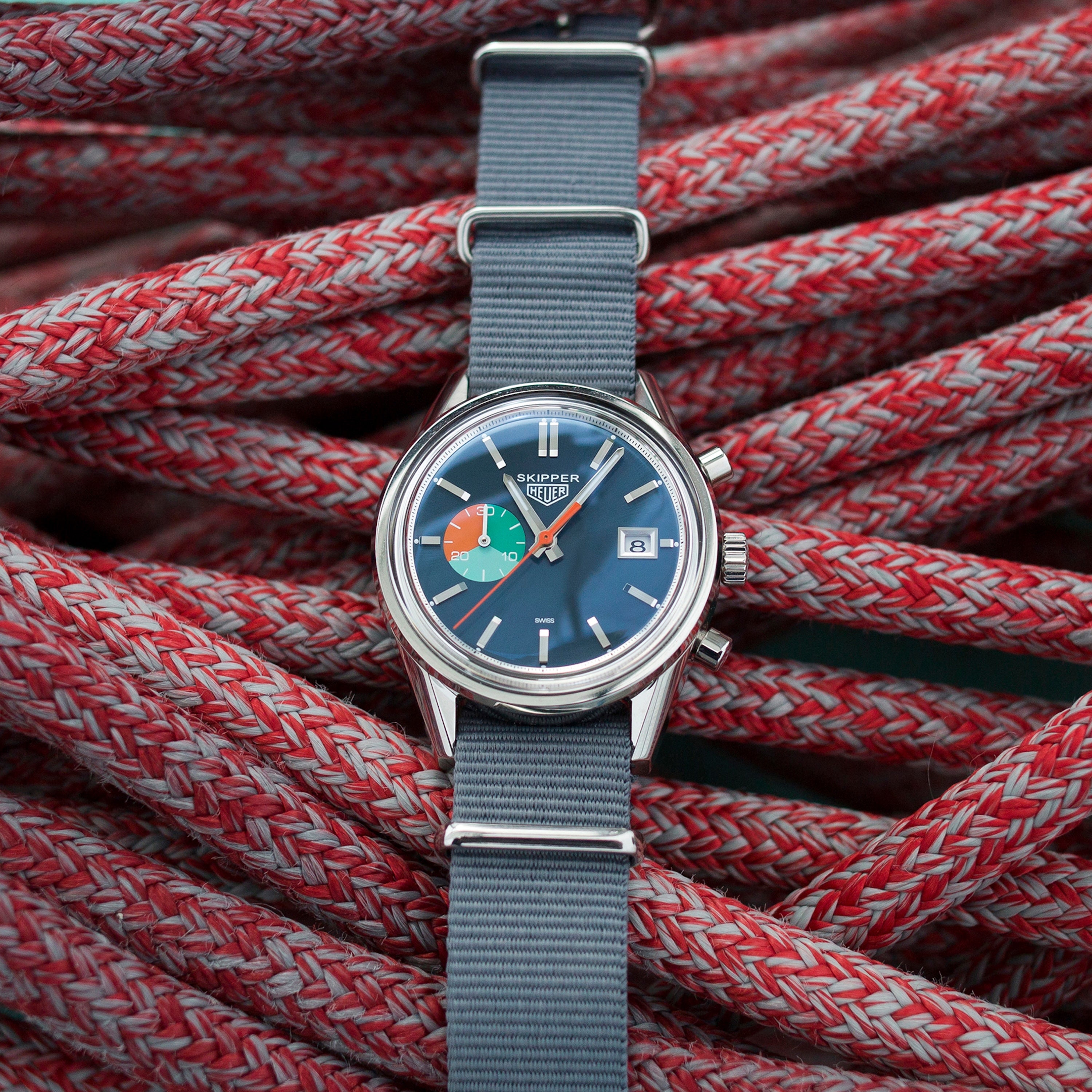 The TAG Heuer Limited Edition Carrera Skipper For HODINKEE, featuring a blue dial and grey strap, rests on coiled red and white rope—a striking choice for collectors and vintage chronograph enthusiasts.