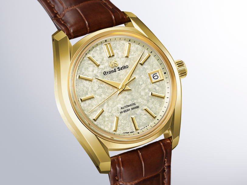 Grand Seiko automatic watch with gold-tone case, cream dial, gold hour markers, and brown leather strap.