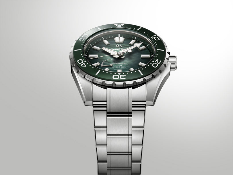 Silver stainless steel diver watch with green dial, black bezel, and matching bracelet on gray background.