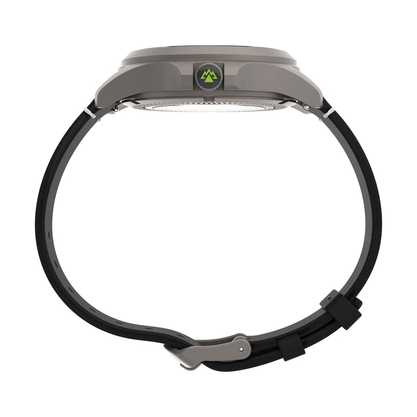 A side view of the Timex Expedition Titanium Automatic shows its gray round case, small green mountain logo on the side, scratch-resistant sapphire crystal, and a black buckle strap curved downward.