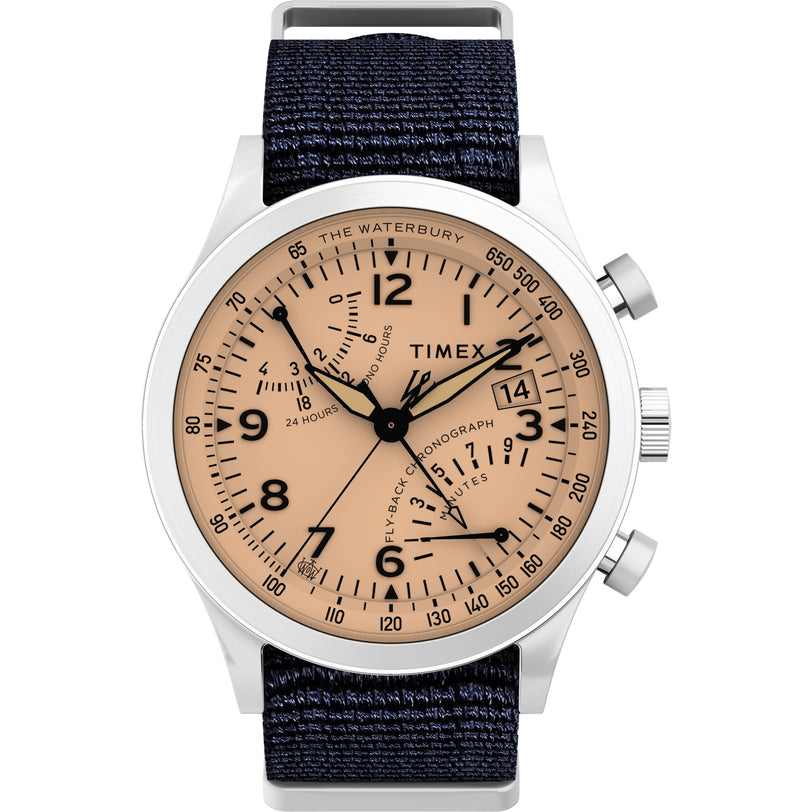 The Timex Waterbury Traditional Fly-Back Chronograph features a beige dial with black markings, three subdials, and a date window in a silver case, paired with a dark blue fabric strap.