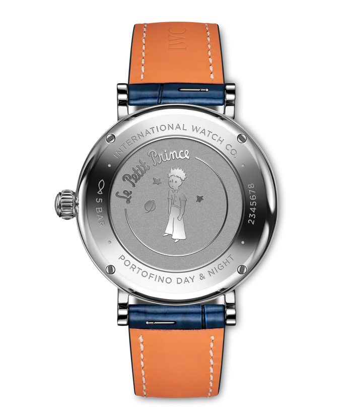Round stainless steel watch with Le Petit Prince illustration on dial, orange and blue leather strap with white stitching.
