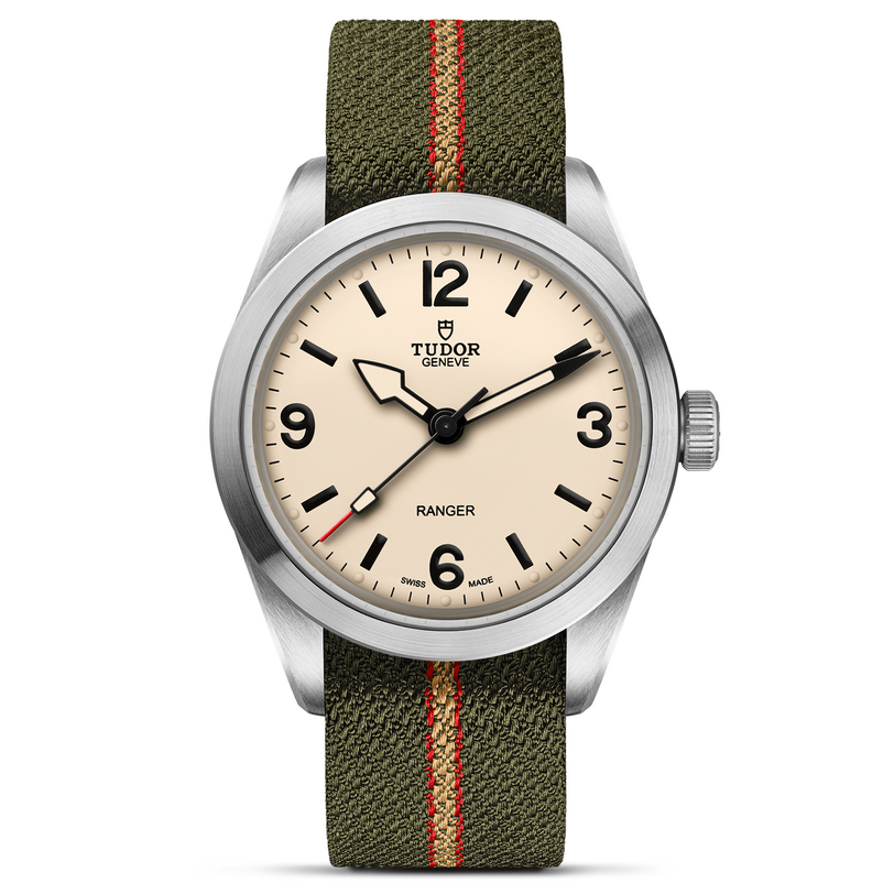 The TUDOR Ranger is an expedition watch with a beige dial, black numerals and hands, and a green fabric strap with a red stripe. A brushed stainless steel case ensures durability for this adventure-ready timepiece.