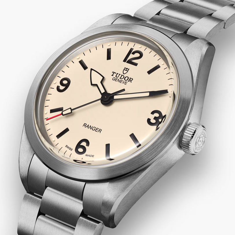 A close-up of the TUDOR Ranger watch featuring a cream dial, bold black numerals, a stainless steel case and bracelet, and black hands with a distinctive red-tipped seconds hand.