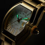 Gold-tone Cartier Roadster watch with barrel-shaped case, white dial, luminous hands, and matching bracelet against black bac