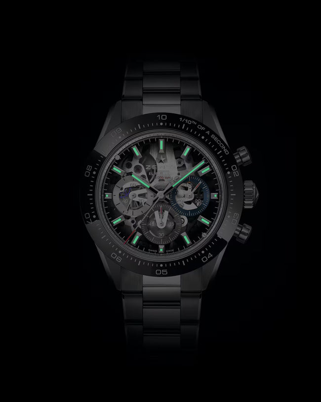 Black stainless steel chronograph watch with skeleton dial, green luminous hands and hour markers, and tachymeter bezel.