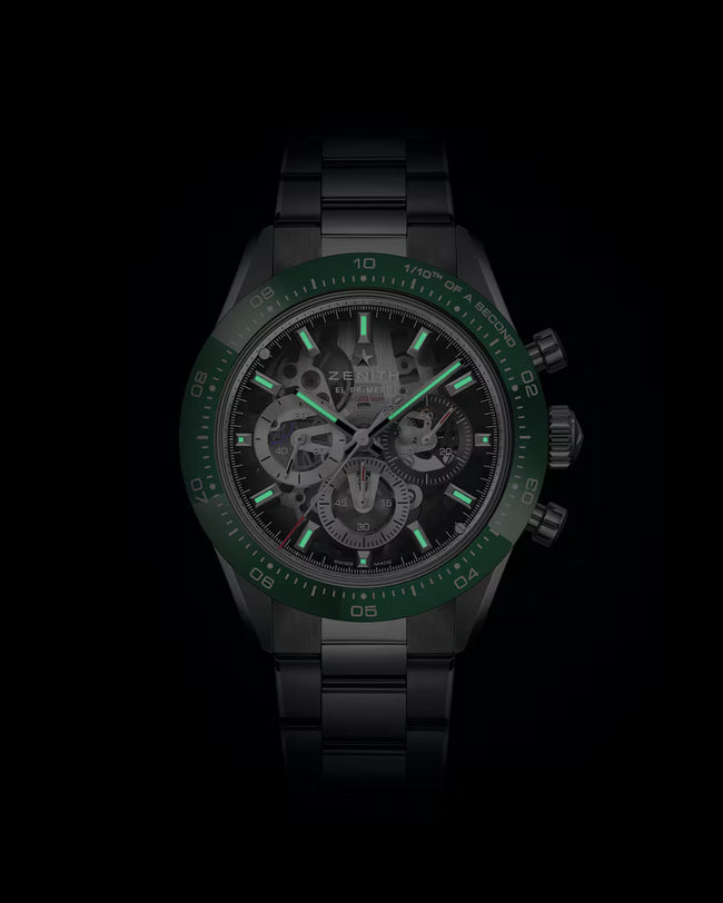 Black sport watch with green bezel, skeleton dial showing exposed gears, luminous hands and hour markers, and metal bracelet.