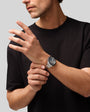 Man wearing black t-shirt with silver chronograph watch on wrist with dark dial and metal band.