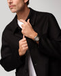 Man wearing black blazer with white shirt, displaying watch on wrist with white dial and brown leather band.