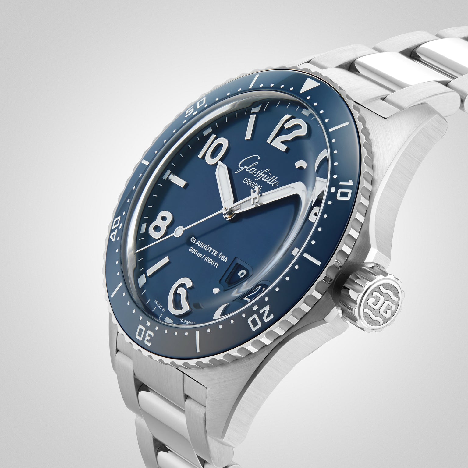 The Glashütte Original SeaQ Panorama Date, a stainless steel wristwatch with a blue dial, bezel, bold white numerals, and a metal bracelet, is shown at an angle to highlight its design against a light background.