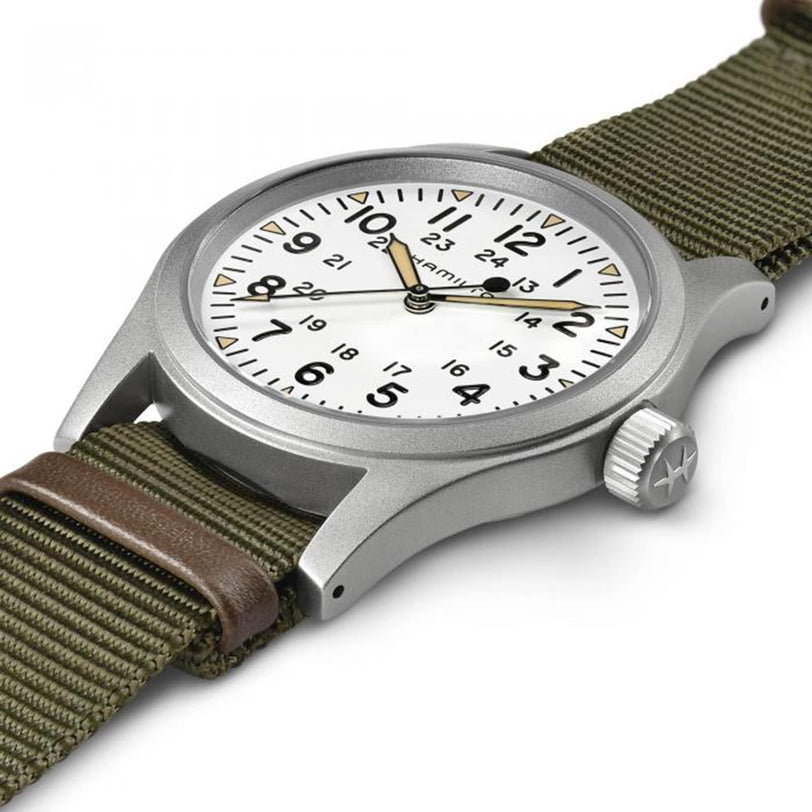 The Hamilton Khaki Field Mechanical, a silver wristwatch with a white dial and green fabric strap, is shown on a white background.