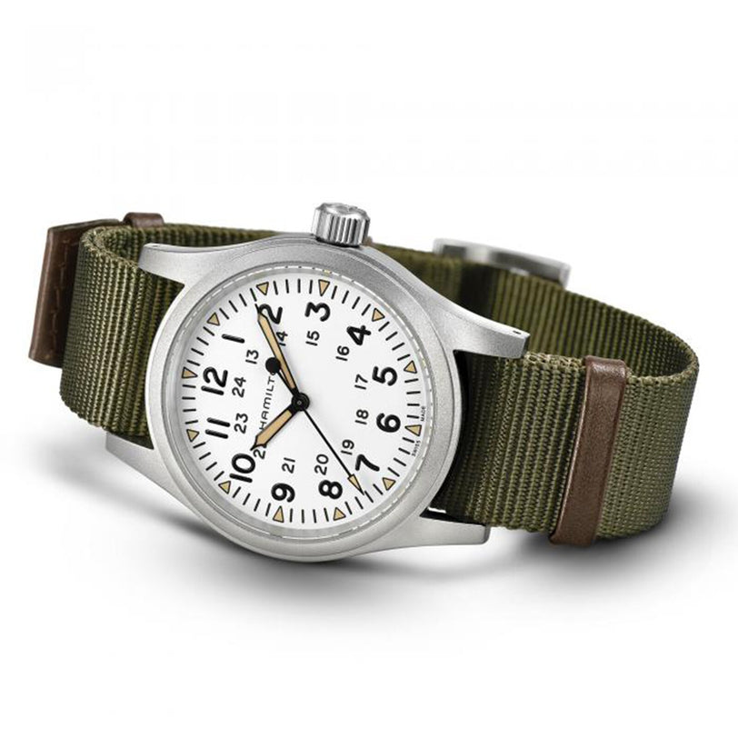 The Hamilton Khaki Field Mechanical is a silver wristwatch with a white face, green fabric strap, and both 12-hour and 24-hour markings.