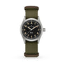 A Hamilton Khaki Field Quartz watch with a black dial and olive green fabric strap is displayed against a white background.