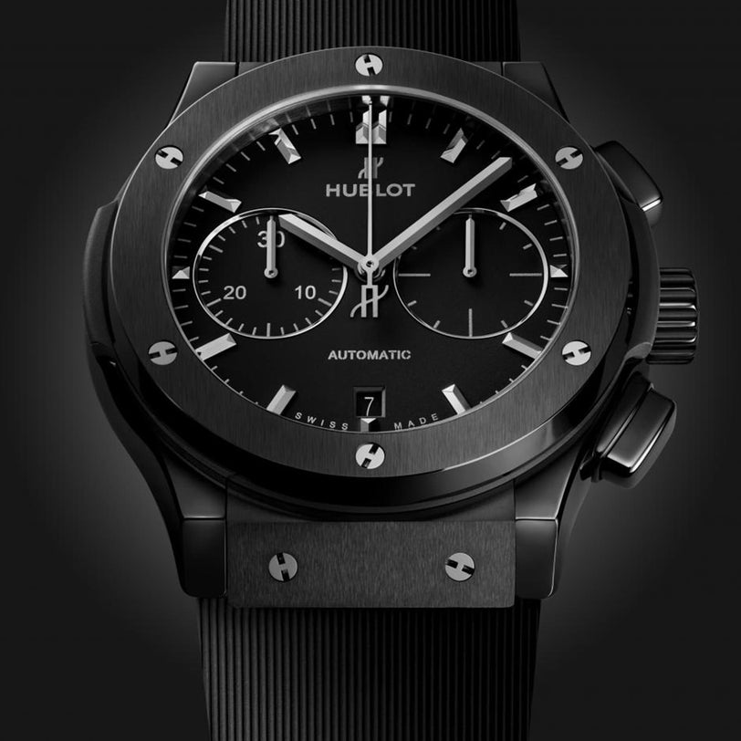 A close-up of the Hublot Classic Fusion Chronograph Black Magic watch featuring a black dial, silver hour markers, subdials, black strap, and a sleek black ceramic case.