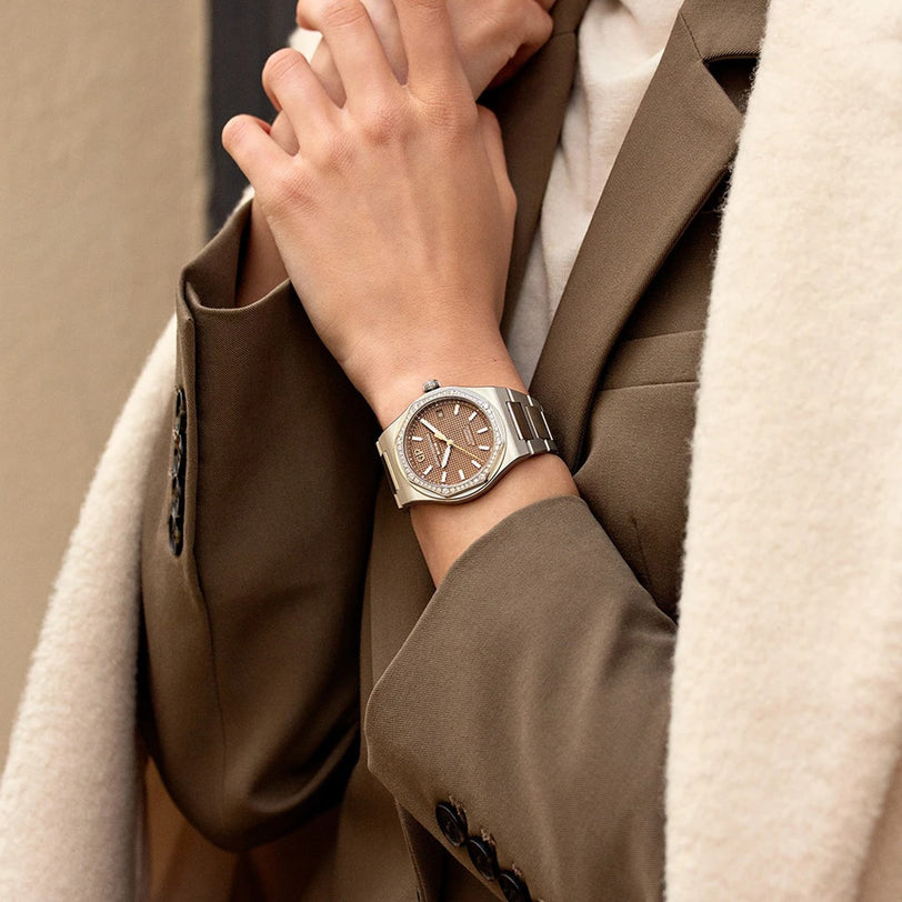 Close-up of a person wearing a silver watch with a brown face, dressed in a beige coat.