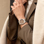 Close-up of a person wearing a silver watch with a brown face, dressed in a beige coat.