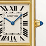 Close-up of a Cartier Tank Louis Medium Model watch face with black Roman numerals, blue sword-shaped hands, gold frame, and blue cabochon crown. CARTIER and SWISS MADE are printed on the dial—a timeless creation by Cartier.