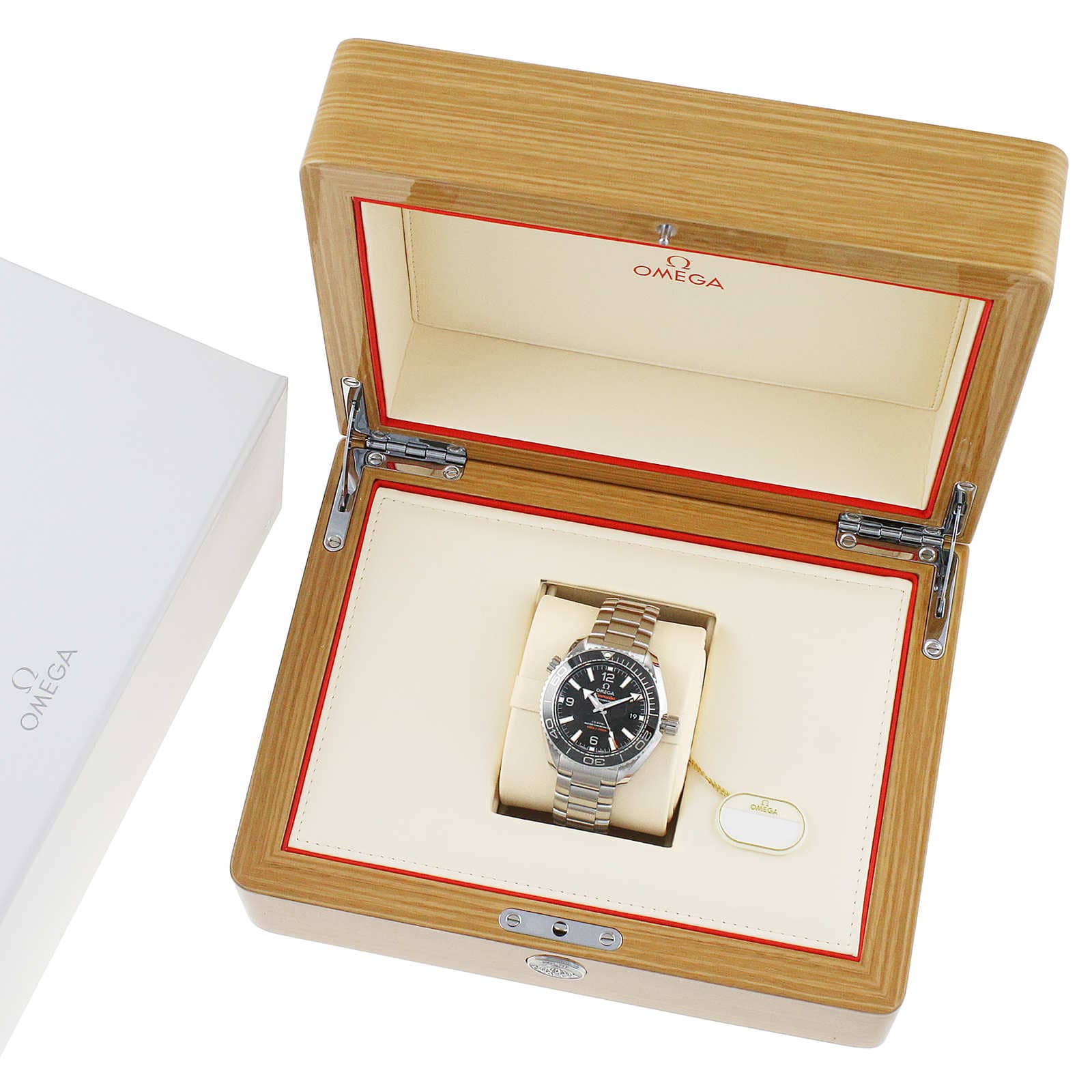 An OMEGA Seamaster Planet Ocean 600M watch is shown inside an open wooden OMEGA box with a cream interior and red trim, placed next to a white box featuring the OMEGA logo.