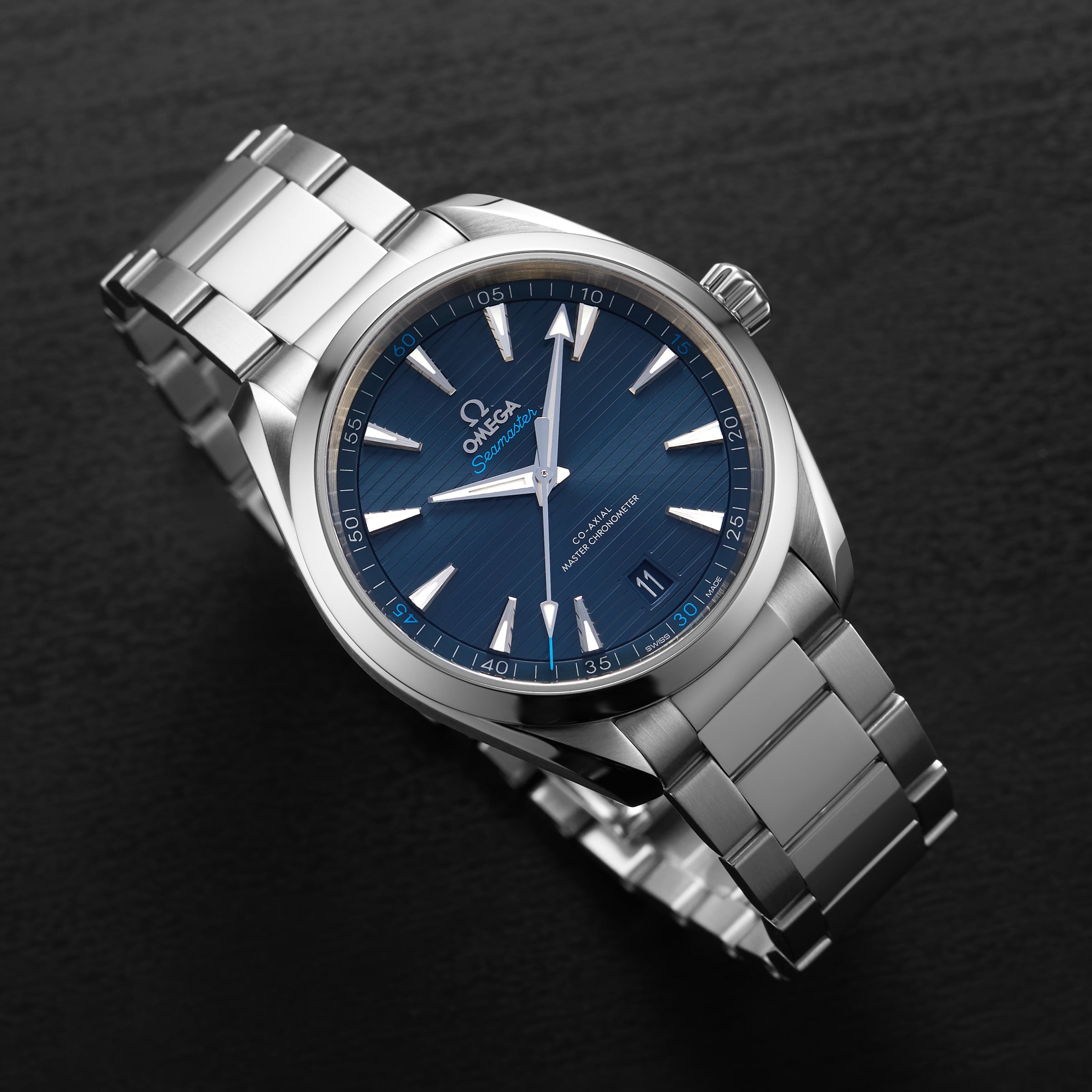 An OMEGA Seamaster Aqua Terra 150M wristwatch with a blue dial, silver hour markers, and stainless steel bracelet is shown on a black surface.