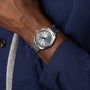 A person in a blue shirt wears the OMEGA Seamaster Aqua Terra 150M, a stainless steel wristwatch with a silver dial and blue hour markers, inspired by Seamaster heritage.