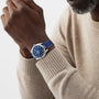A person in a beige sweater showcases an OMEGA Seamaster Aqua Terra 150M with a blue dial and matching blue strap on their left wrist.