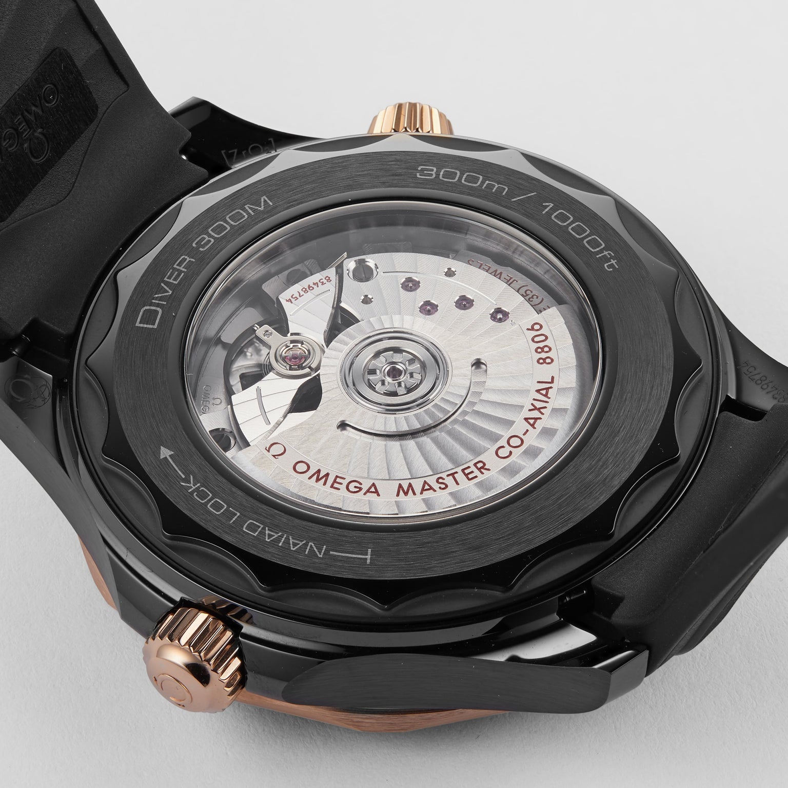 Close-up of the Seamaster Diver 300M by OMEGA, showcasing its intricate Calibre 8806 movement through a transparent case back engraved with detailed specifications.