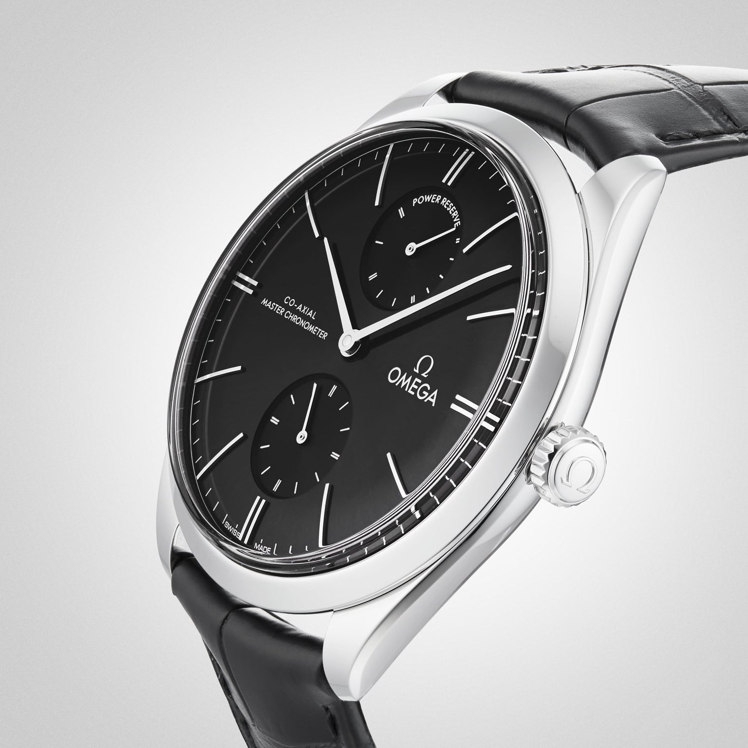 A close-up of the OMEGA De Ville Trésor showcases its black dial with two subdials, silver hour markers, and a black leather strap, all set in a 40mm stainless steel case against a light gradient background.