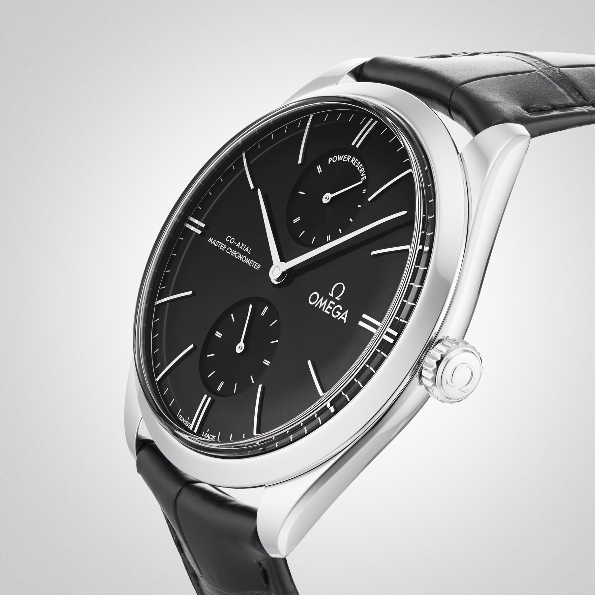 A close-up of the OMEGA De Ville Trésor showcases its black dial with two subdials, silver hour markers, and a black leather strap, all set in a 40mm stainless steel case against a light gradient background.