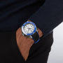 Someone wears an OMEGA Seamaster Planet Ocean 6000M wristwatch with a blue and white face and black band, famed for its water resistance, as their hand rests in the pocket of dark pants.