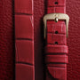 Close-up of the OMEGA De Ville Mini Trésors red leather strap with a gold buckle, set on textured red leather, highlighting its elegant design and signature 18K Moonshine™ Gold detailing.
