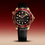 An OMEGA Seamaster Diver 300M wristwatch with a bronze gold case, burgundy bezel, and black rubber strap, featuring the Master Chronometer Calibre 8806, set against a gradient red-to-beige background.